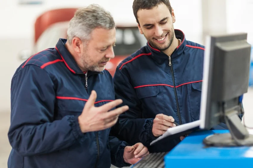 two mechanics in the heavy-duty repair service consulting in front of a computer in their shop